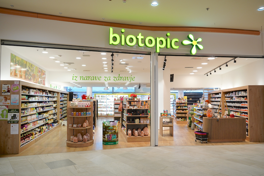 A bright, inviting health store entrance with shelves of products, wooden accents, and a green "biotopic" sign.