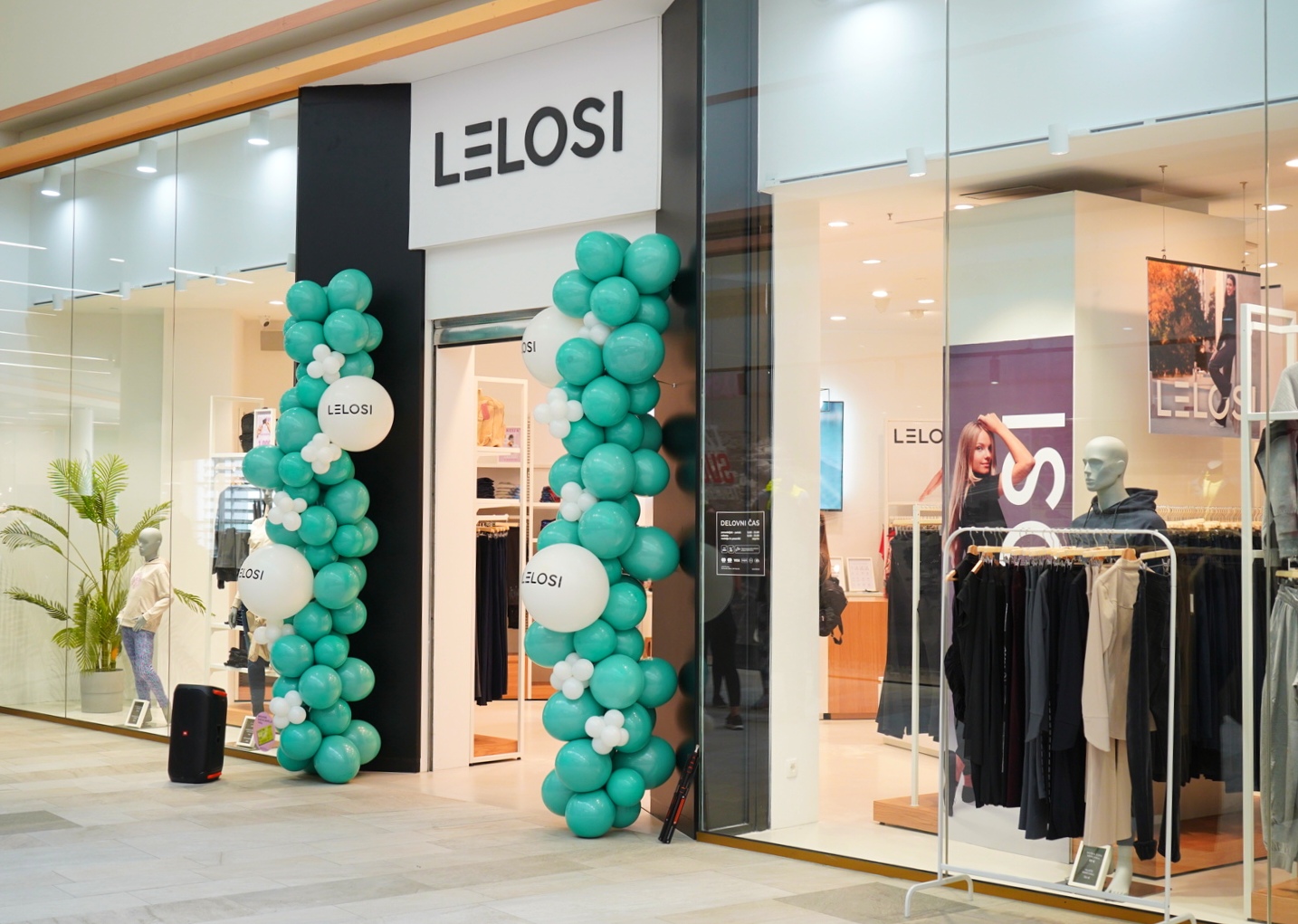 A storefront with the name "LELOSI," decorated with teal and white balloons, showcasing clothing inside.