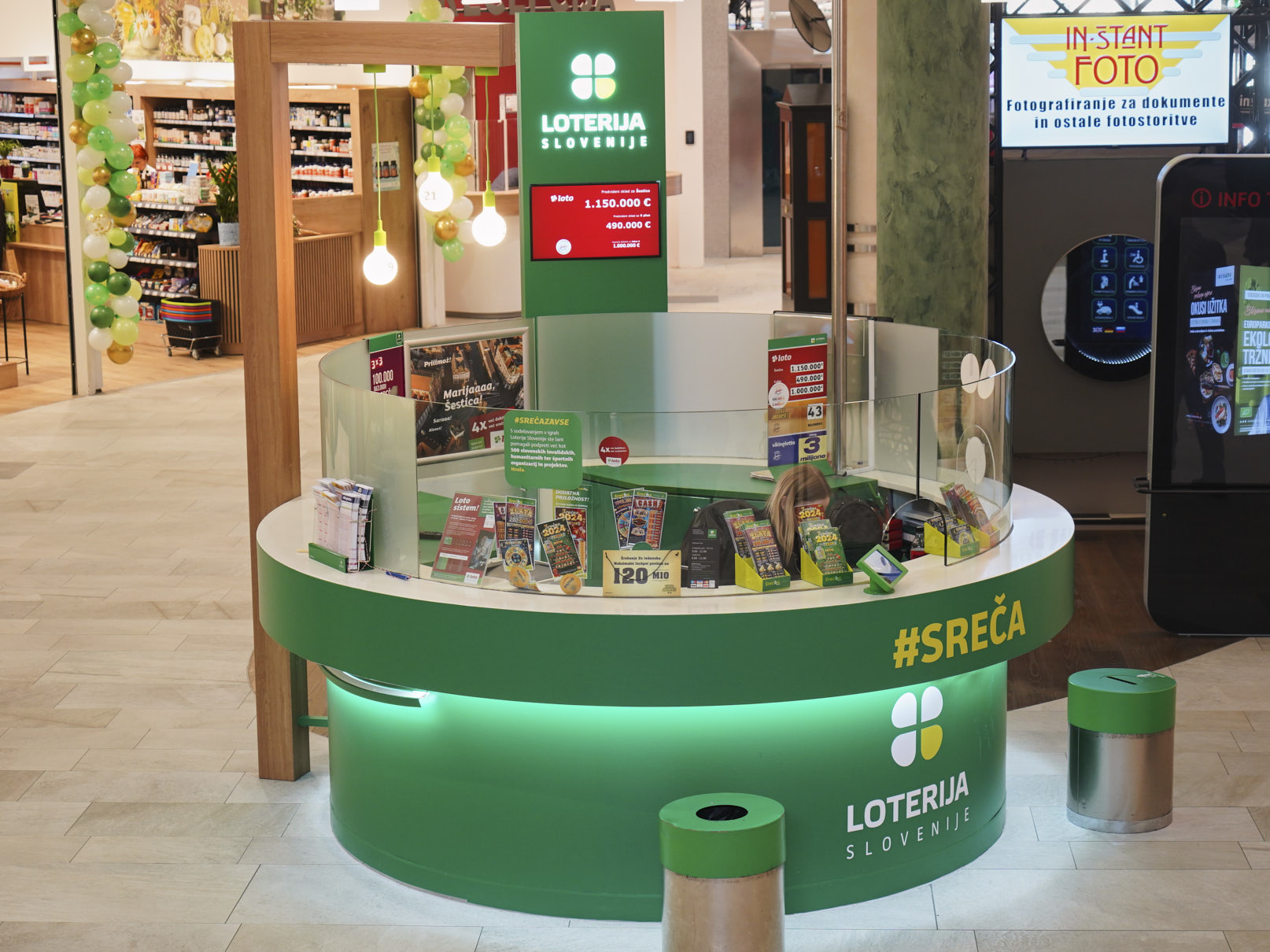 A lottery kiosk with a green design, displaying tickets and promotional materials, in a retail environment.