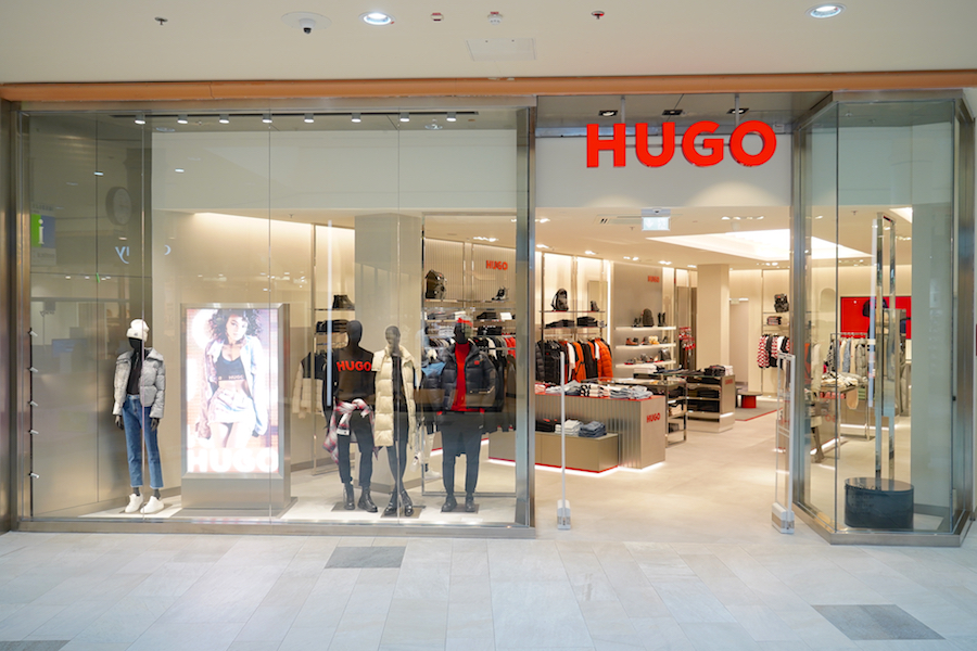 A storefront displaying the "HUGO" brand, featuring mannequins in stylish clothing and a bright interior with various apparel.