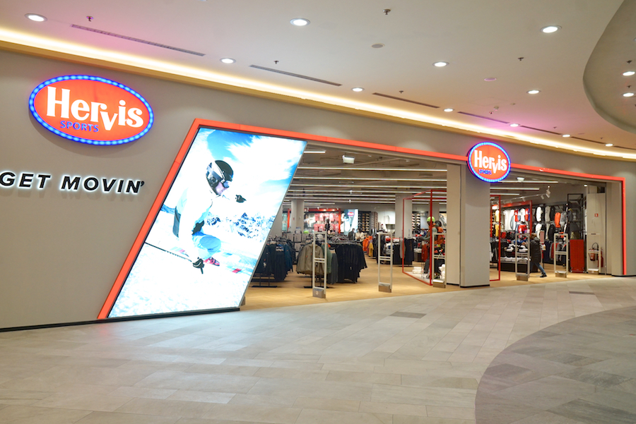 A sports store entrance featuring a large display, bright signage, and a variety of athletic clothing visible inside.