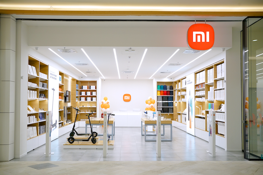 A modern retail store with a white and wooden interior, featuring Xiaomi products, displays, and a prominent logo.