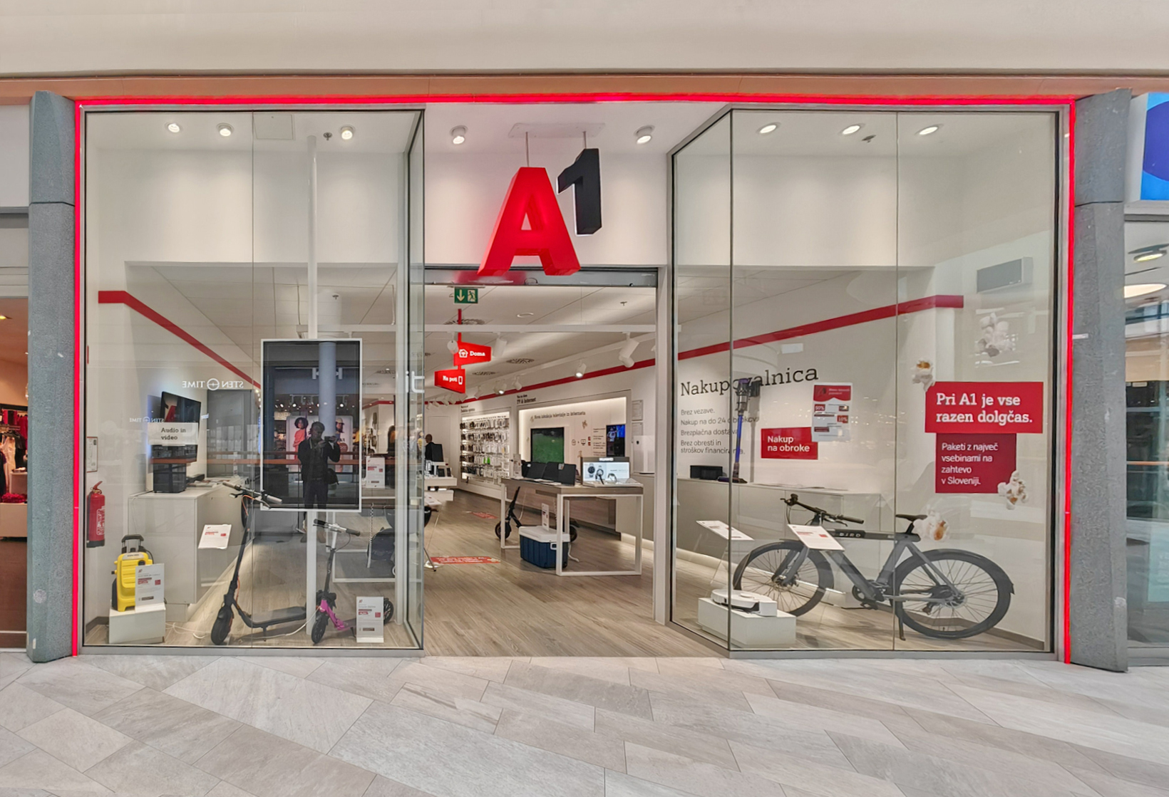 A modern retail store entrance with large glass doors, featuring the logo "A1" and displays of scooters and bicycles inside.