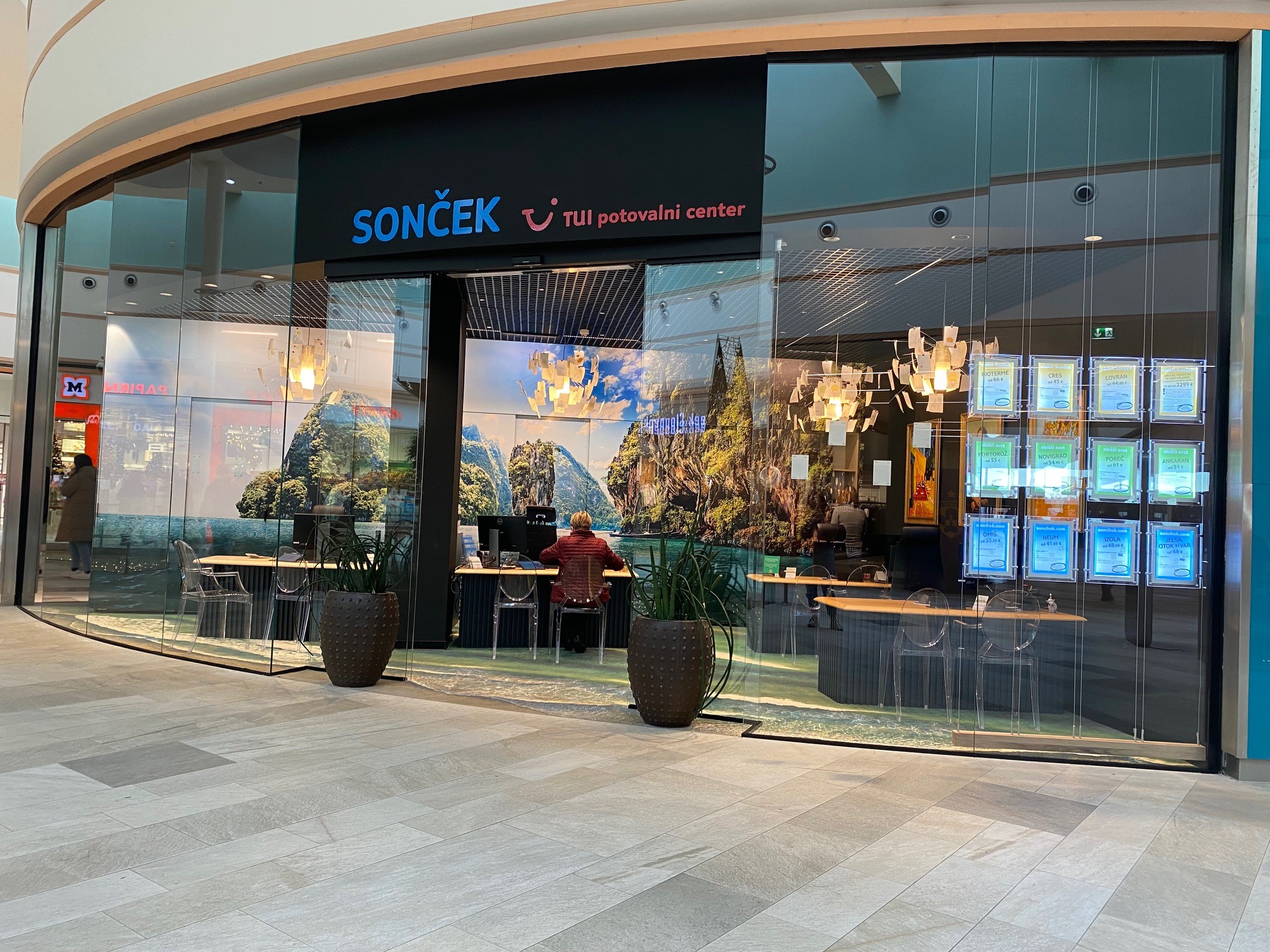 A travel agency storefront with glass walls, featuring a scenic backdrop, seating, and illuminated certificates on display.