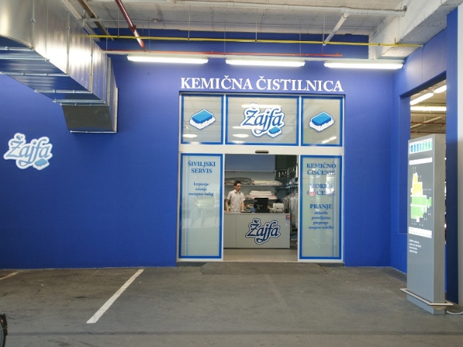 A blue storefront with the name "Žafa" prominently displayed, featuring a window and a sign for a dry cleaning service.