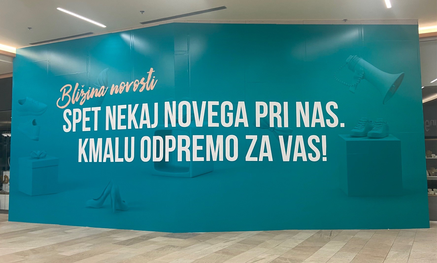 A large promotional wall with teal background and white text announcing new arrivals, featuring images of shoes and a gift box.