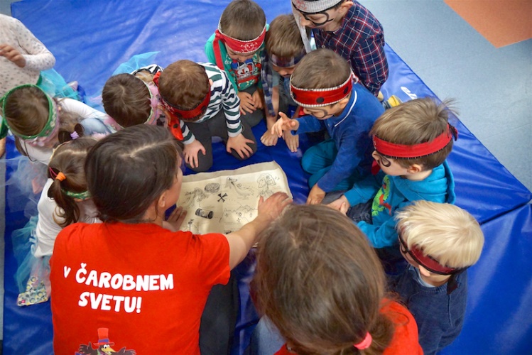 A group of children wearing blindfolds gathers around an adult, examining a map on a blue mat.