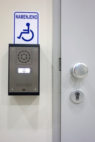 A wall-mounted intercom system next to a door with a blue accessibility sign above it.