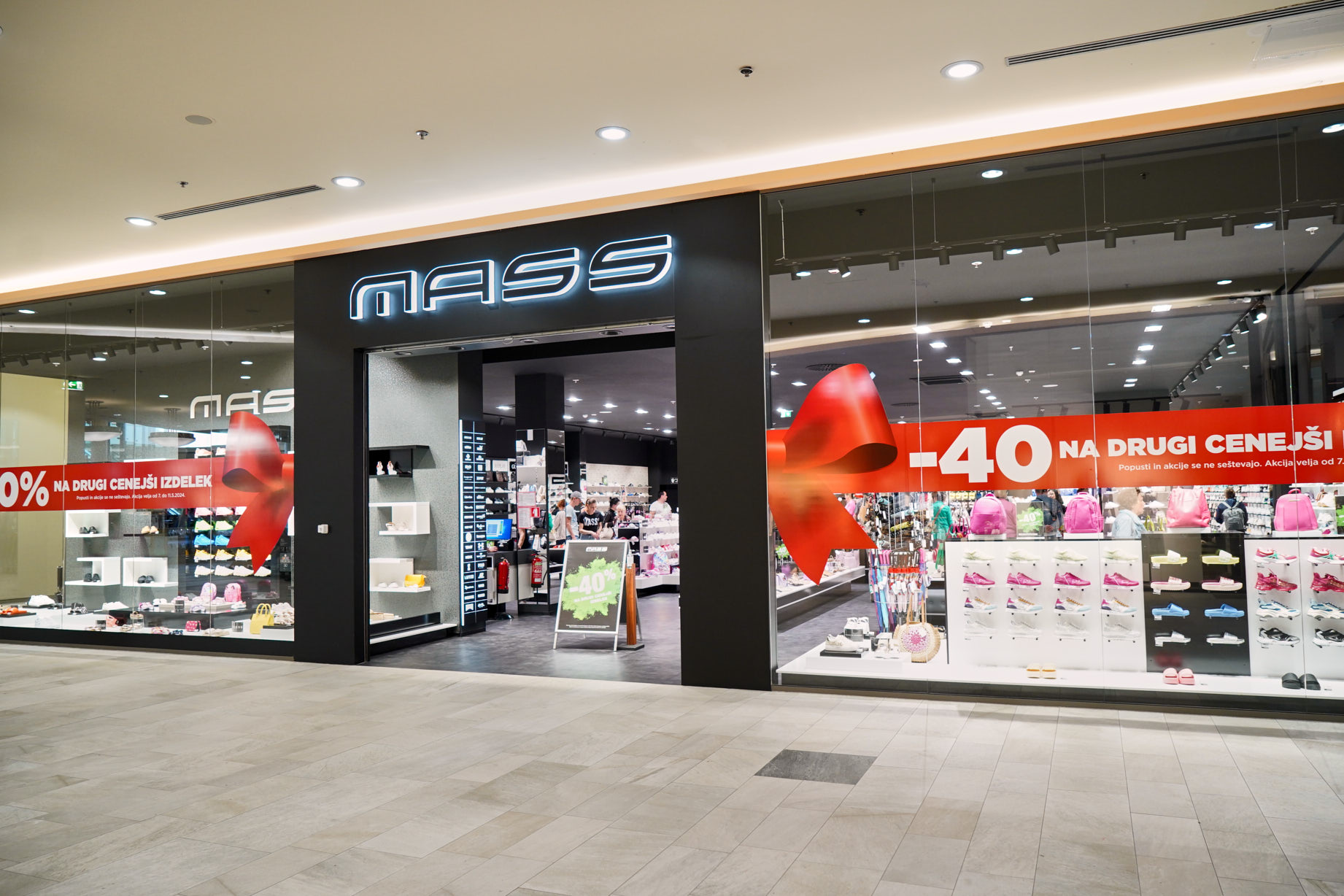 A retail store named "MASS" with a large red sale sign displaying discounts. The entrance showcases various footwear and accessories.