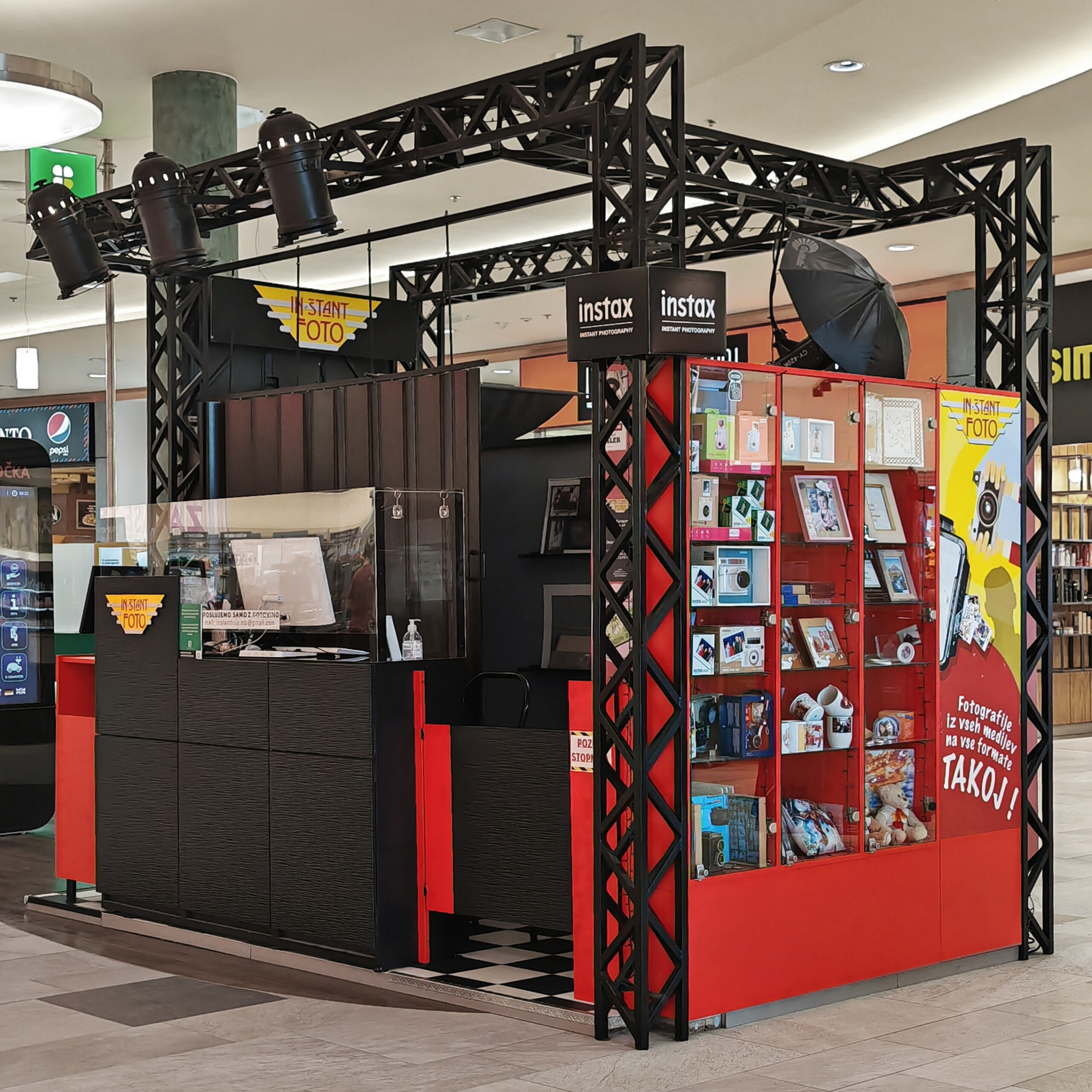 A photo booth kiosk with a black and red design, featuring instant photography equipment and displays of photo-related products.