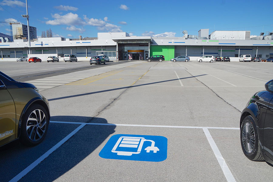 A parking lot with electric vehicle charging spots, featuring two parked cars and a large building in the background.