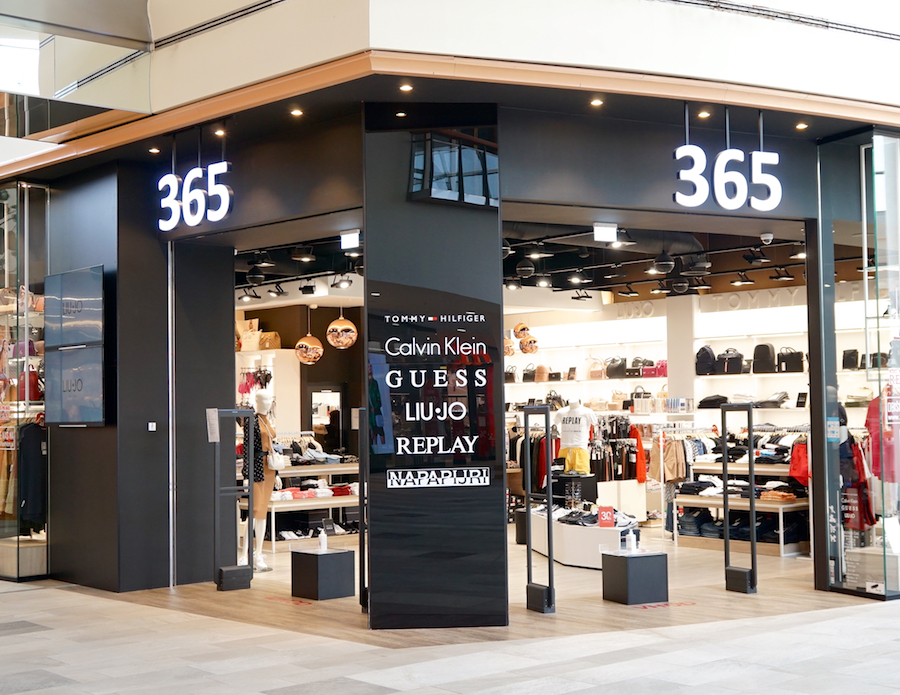 A retail store entrance featuring brands like Calvin Klein, Guess, and Replay, with a modern design and bright signage.