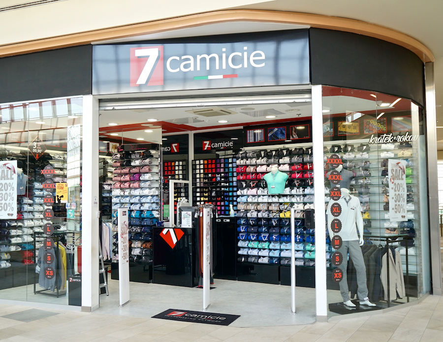 A clothing store named "7 camicie" featuring a variety of shirts displayed on racks and mannequins, with sale signs visible.