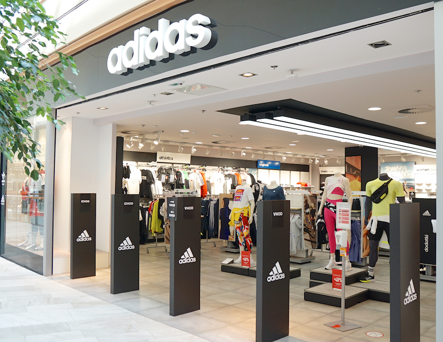 An Adidas store entrance featuring athletic apparel displays and mannequins, with a prominent logo above.