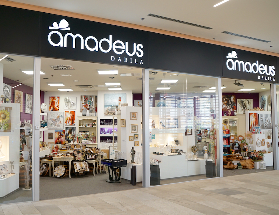 A storefront displaying "Amadeus Darila," featuring art, decor, and various gifts inside.