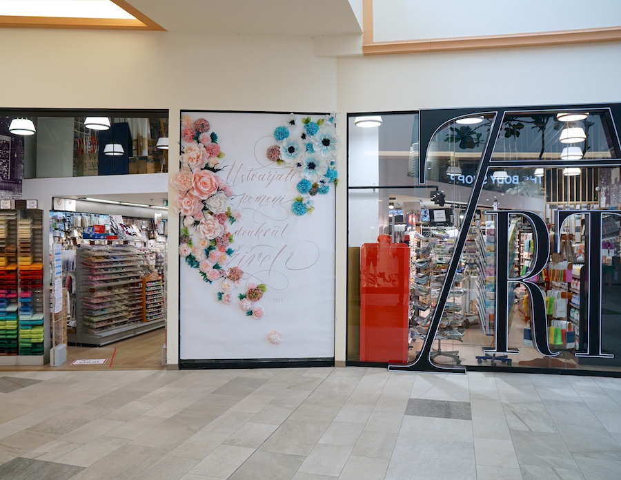 A decorative wall with flowers and elegant lettering, next to a store displaying colorful craft supplies.