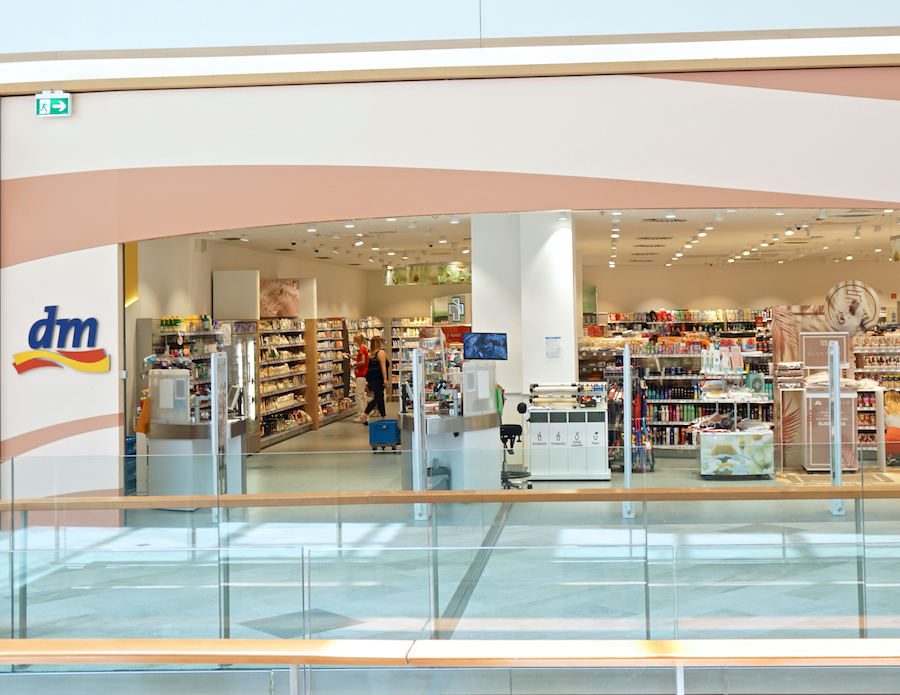 A view of a dm store with shelves stocked with various products, featuring a checkout area and customers browsing inside.