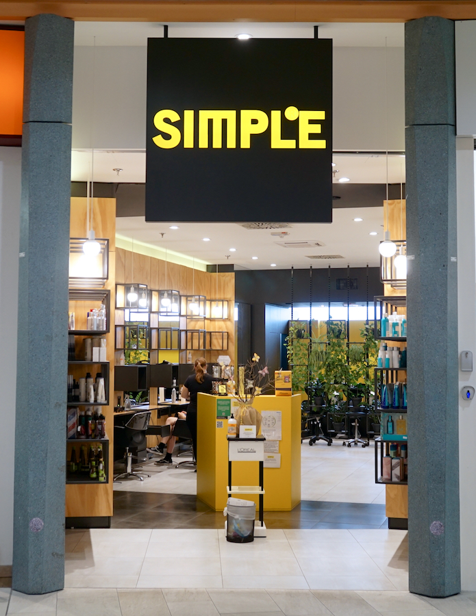 A salon entrance with a large "SIMPLE" sign. Inside, there are workstations, plants, and shelves of hair products.