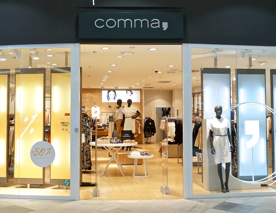 A clothing store entrance featuring mannequins, stylish apparel, and a 50% off sign. Brightly lit interior with modern decor.