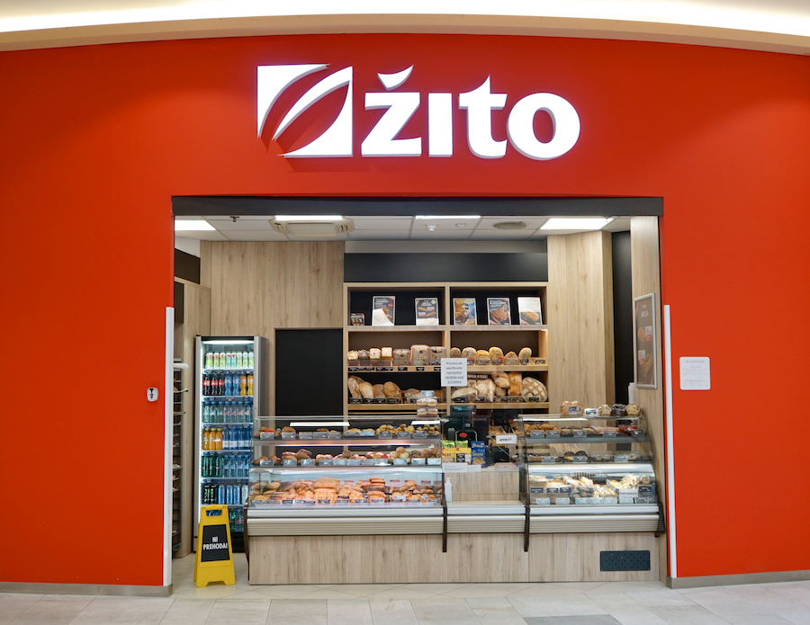 A bakery shop with a red wall, featuring a display of various breads and pastries behind glass.