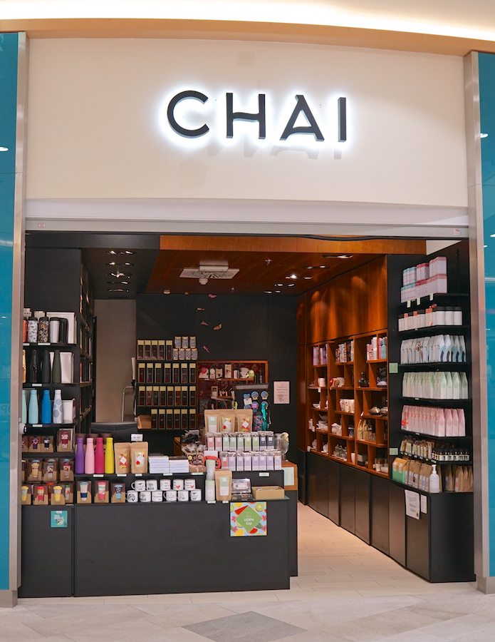 A storefront labeled "CHAI" featuring shelves of colorful products, tea, and accessories, with a modern design and warm lighting.