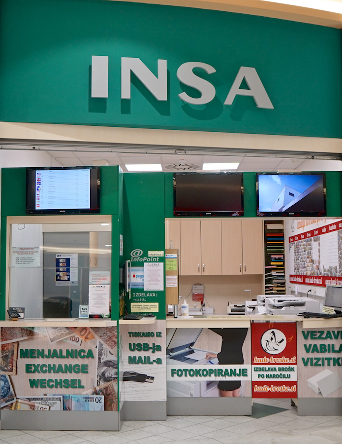 A service counter with the sign "INSA," offering currency exchange and photocopying services, with multiple screens above.