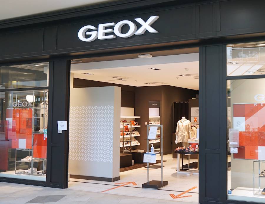 Storefront of a GEOX shop featuring shoes and clothing displays, with a modern design and clear signage.