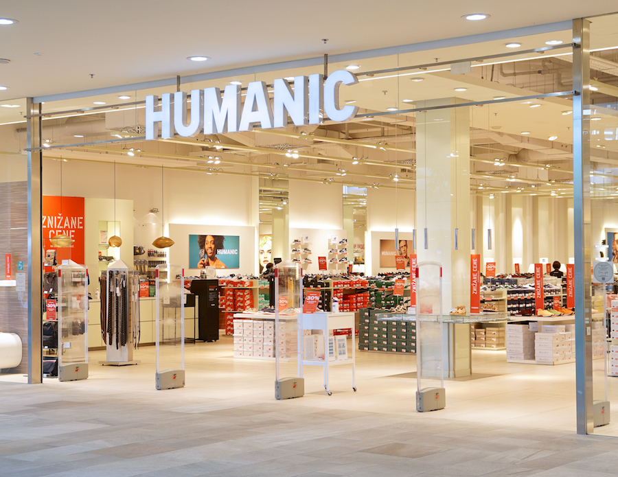 A retail store entrance with the sign "HUMANIC." Inside, shelves display various shoe boxes and promotional signs.