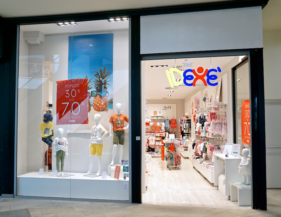 A children's clothing store entrance featuring mannequins in colorful outfits and promotional signs for discounts.