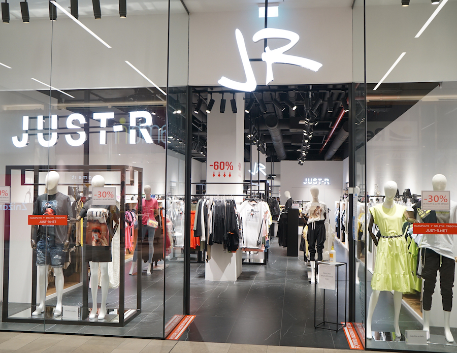 A modern clothing store entrance featuring mannequins, sale signs, and a stylish interior.