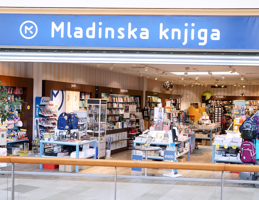 A bookstore entrance with the sign "Mladinska knjiga," showcasing shelves of books and various stationery items inside.