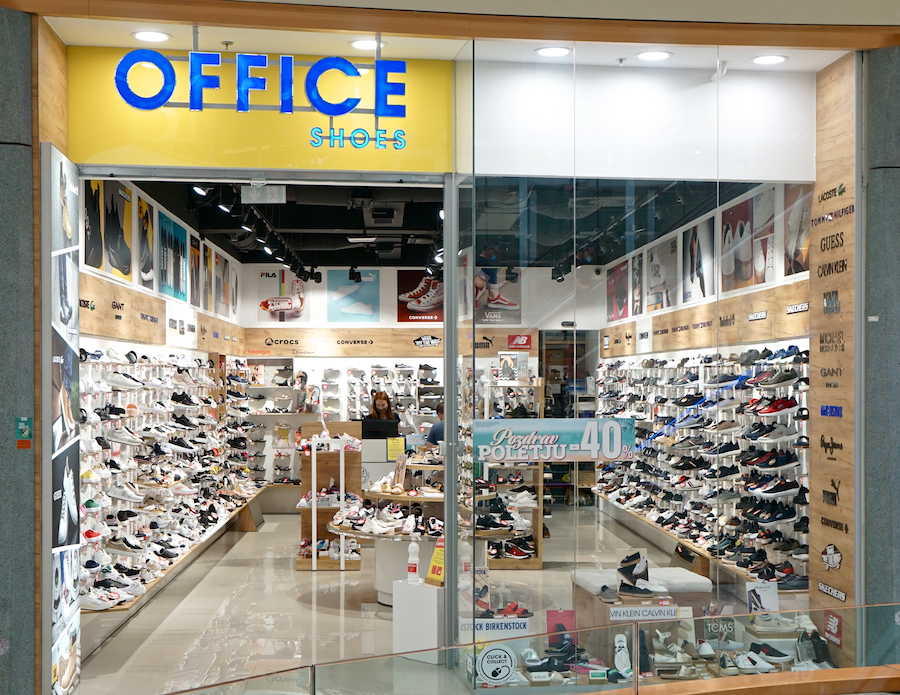 A shoe store display featuring various sneakers and footwear, with a prominent "OFFICE SHOES" sign and a sale banner.