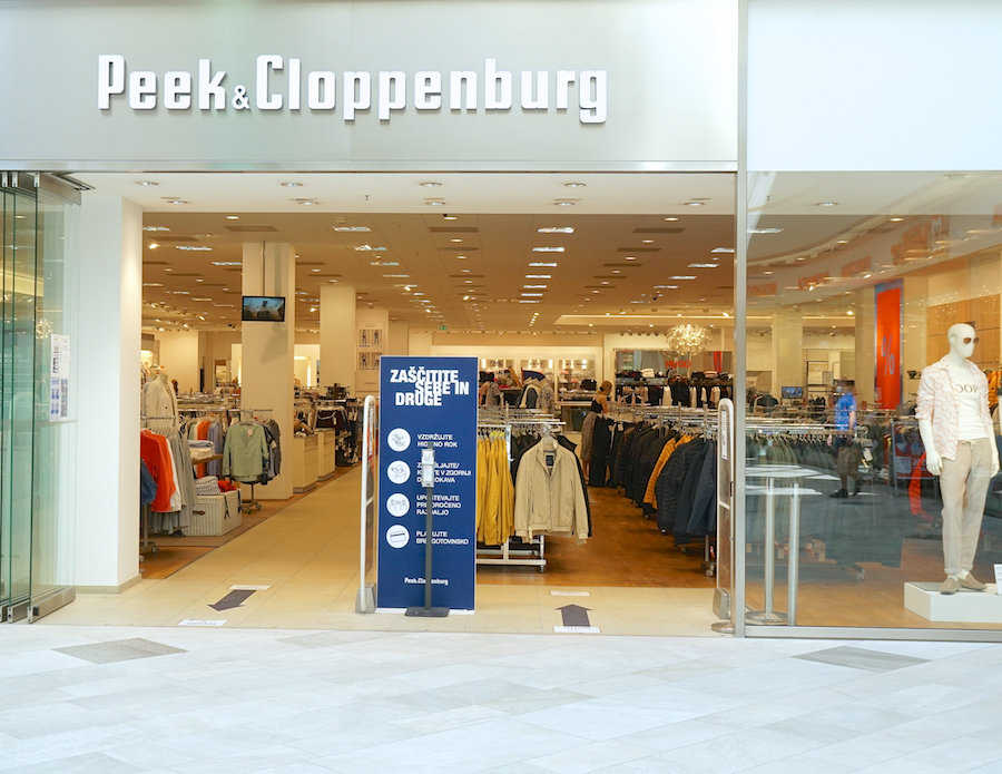 A storefront of Peek & Cloppenburg featuring clothing displays and a sign with safety guidelines.