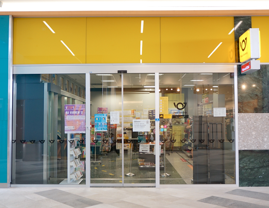 A storefront with glass doors, featuring a yellow upper section and various signs inside, indicating a postal or retail service.