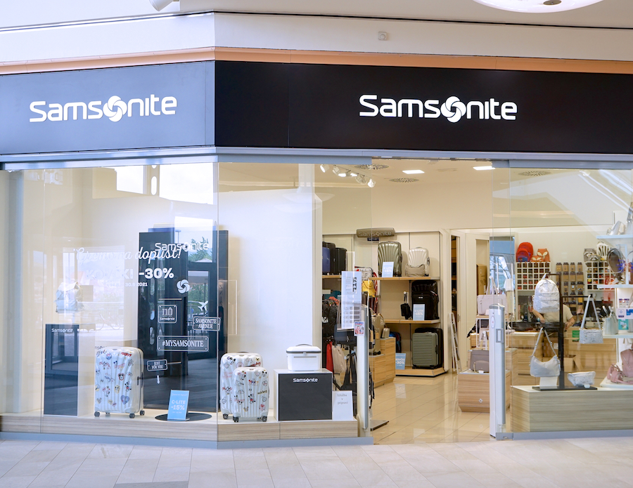 A storefront displaying Samsonite luggage and accessories, featuring promotional signs and various bags inside.