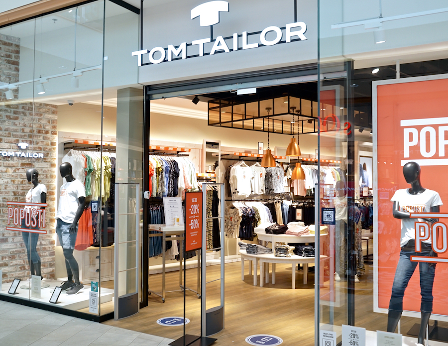 A storefront of Tom Tailor featuring mannequins in casual clothing and a display of various apparel inside.