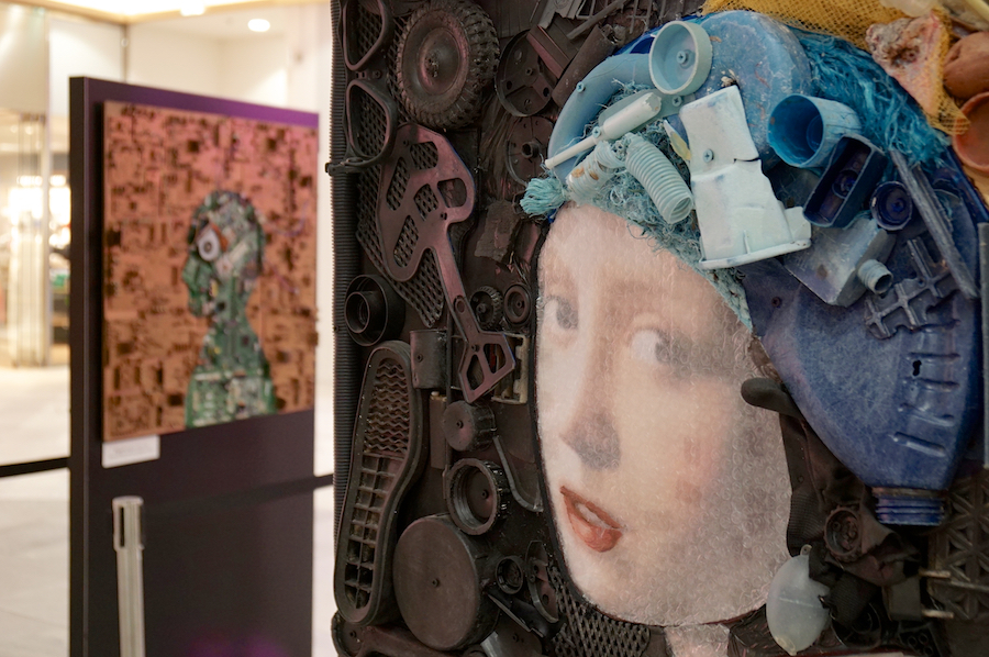 An artistic installation featuring a face made of various materials, with another abstract piece in the background.