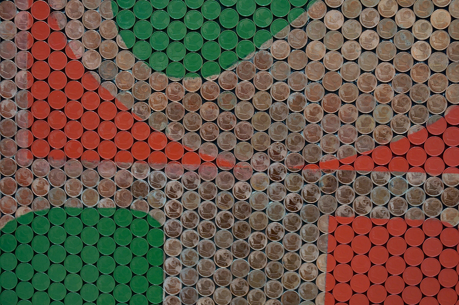 A colorful mosaic made of circular cans in red, green, and brown, arranged in geometric patterns.