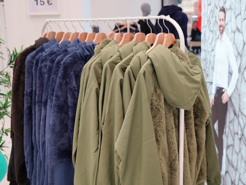 A rack displaying various hooded jackets in dark blue, green, and brown colors, with a price tag of 15€.